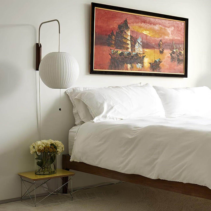 Globe Bubble Ball wall sconce beside a white bed beneath colorful framed artwork