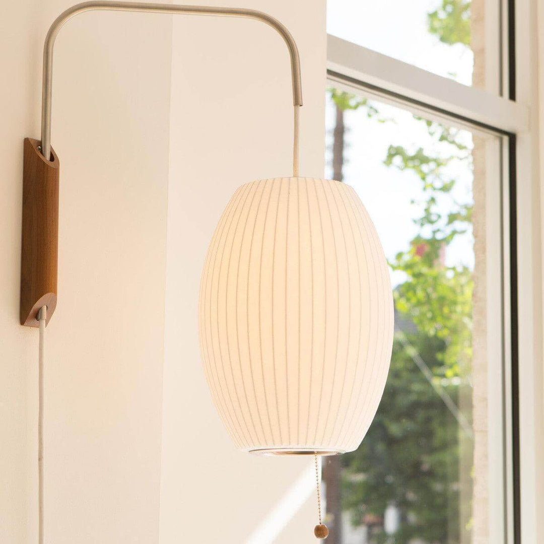 Illuminated oval Bubble Ball wall sconce with a walnut base beside a bright window