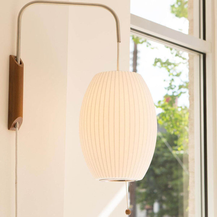 Illuminated oval Bubble Ball wall sconce with a walnut base beside a bright window