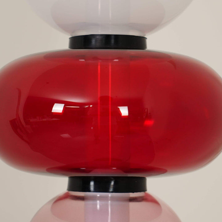 Close-up of the glossy red hand-blown glass accent between the pale and smoky glass shades.