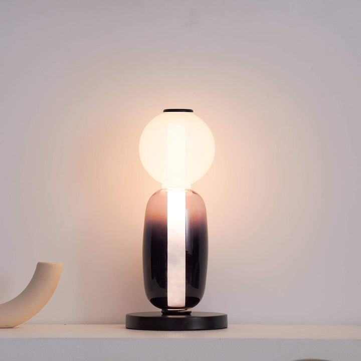 Decorative smoked glass table lamp with a clear globe styled beside orange fabric and dried flowers