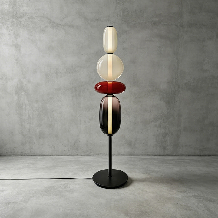 Standard-height Candied Model A Red floor lamp glowing against a textured gray concrete wall.
