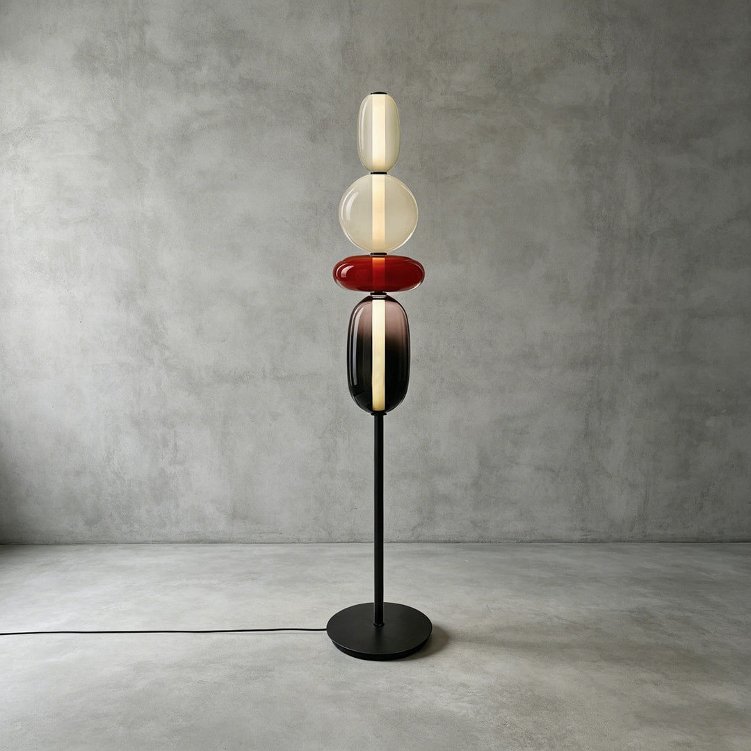 Tall Candied Model A Red glass floor lamp with a warm illuminated core against a concrete wall.