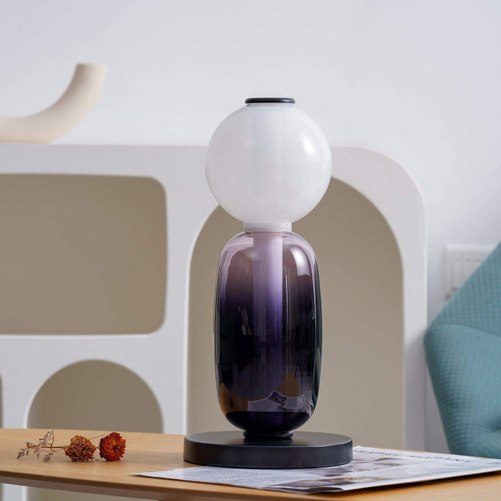 Warm LED accent lamp with glowing white globe and dark gradient glass body on a display shelf