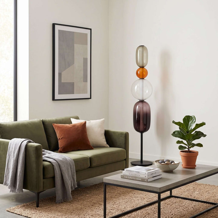 Unlit Candied Model B Orange glass floor lamp beside a green sofa in a modern living room.