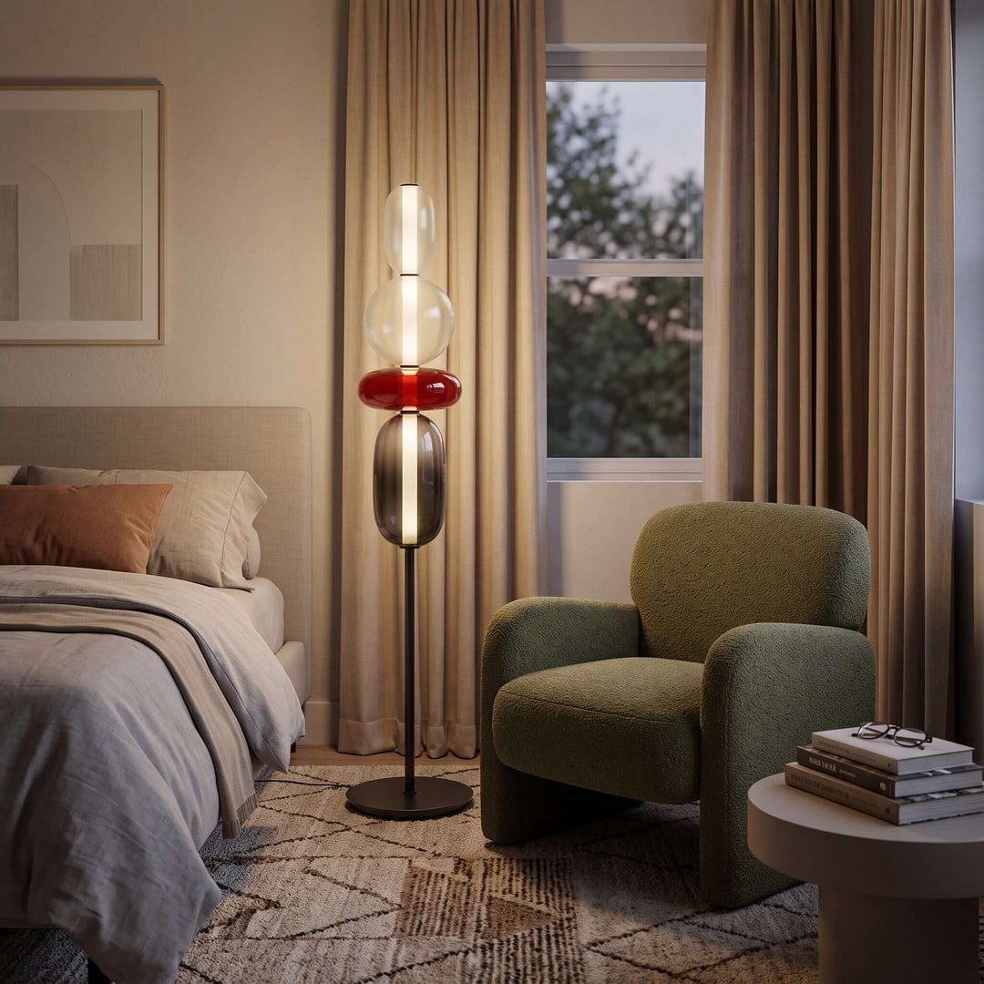 Candied red glass floor lamp glowing beside a green armchair and upholstered bed in a cozy bedroom.