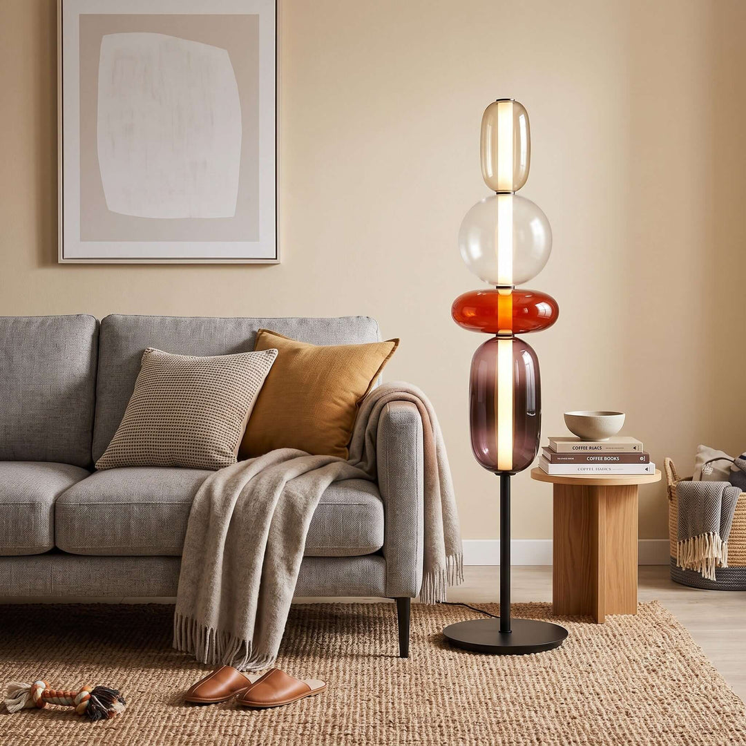 Candied red glass floor lamp casting a warm glow beside a gray sofa and wood side table.