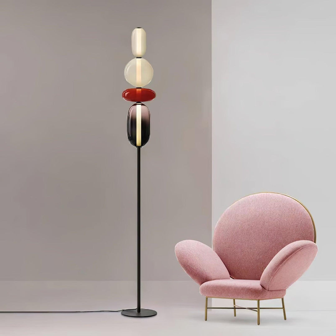 Candied red glass floor lamp displayed beside a sculptural pink armchair against a pale gray wall.