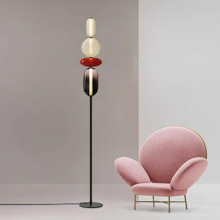 Candied red glass floor lamp displayed beside a sculptural pink armchair against a pale gray wall.