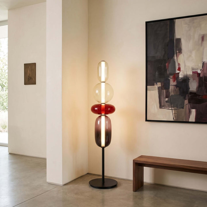 Candied red glass floor lamp displayed beside a wood bench and abstract artwork in a modern entryway.