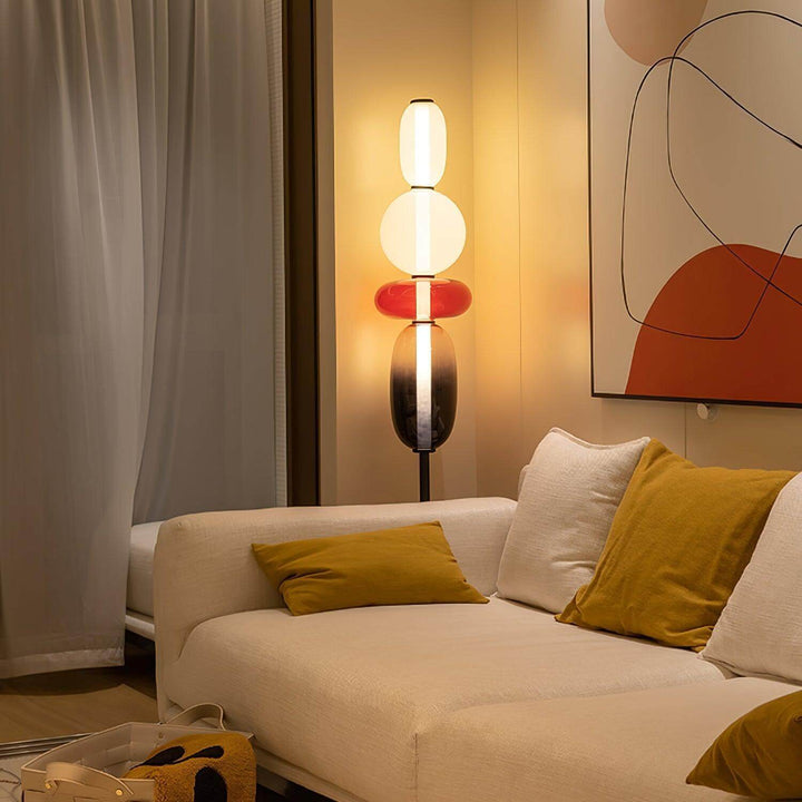 Candied red glass floor lamp illuminating a white sofa with mustard cushions and abstract wall art.