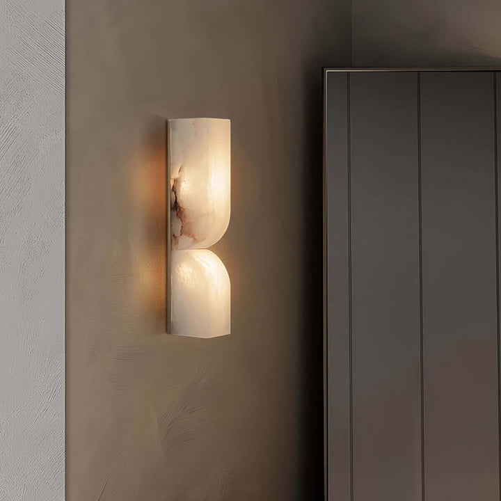 Cavira alabaster wall sconce casting a warm glow beside a tall cabinet in a dark modern interior