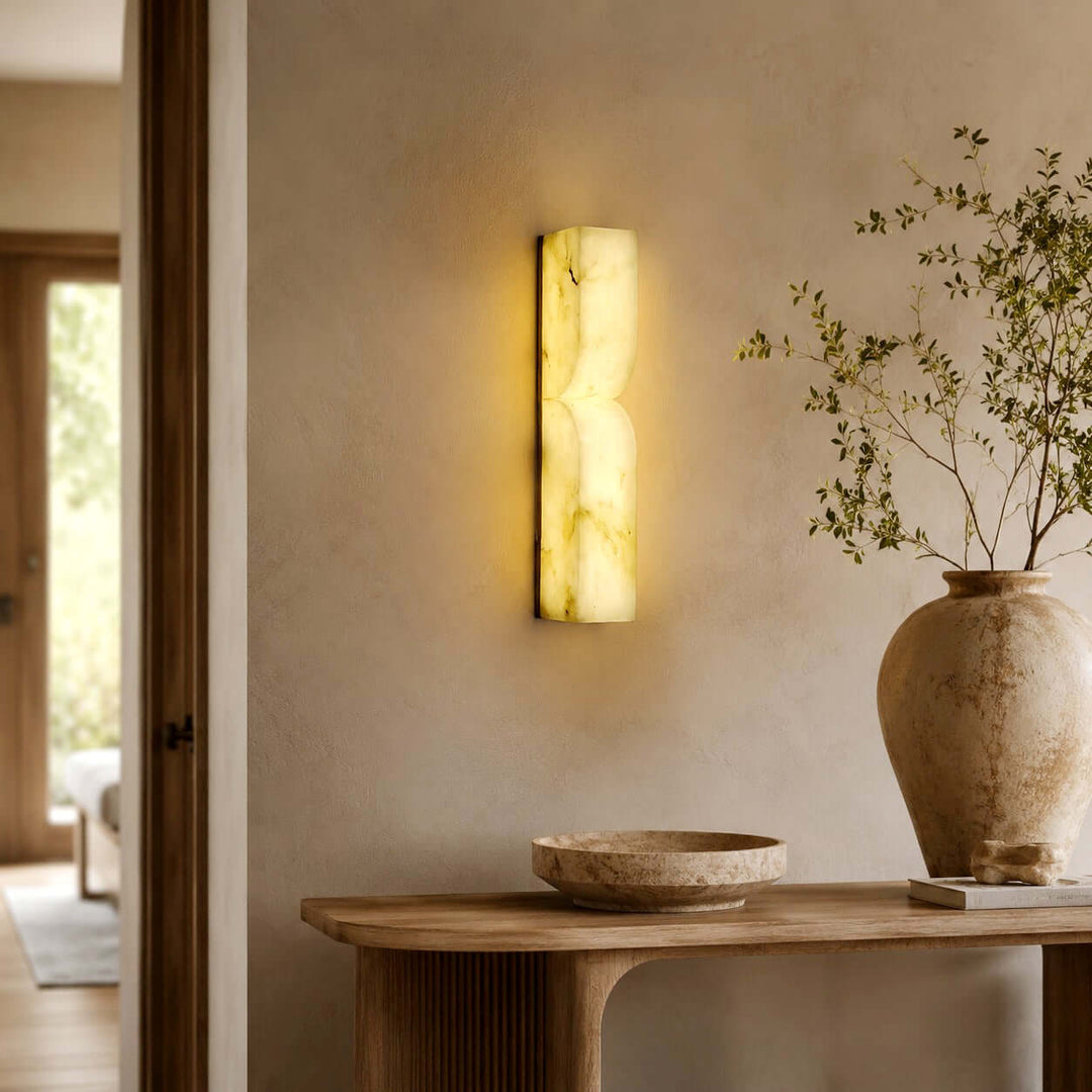 Cavira alabaster wall sconce illuminating a warm entryway above a wood console with natural decor