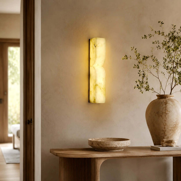 Cavira alabaster wall sconce illuminating a warm entryway above a wood console with natural decor