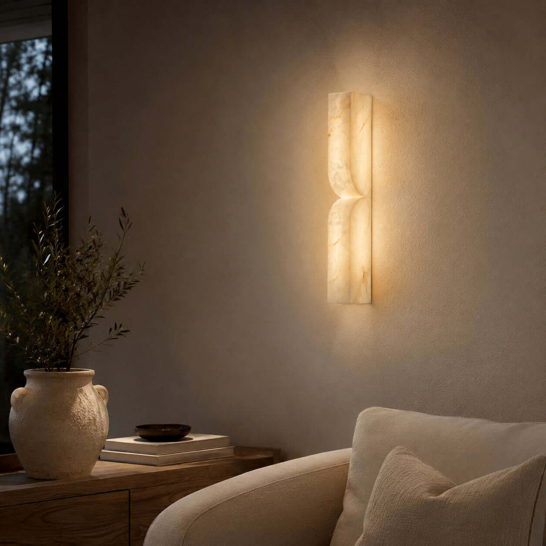 Cavira alabaster wall sconce adding warm ambient light to an evening living room with a neutral armchair