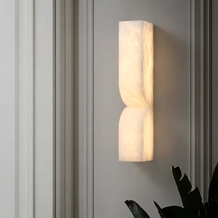 Cavira Wall Sconce with a softly illuminated alabaster surface mounted on a gray paneled wall