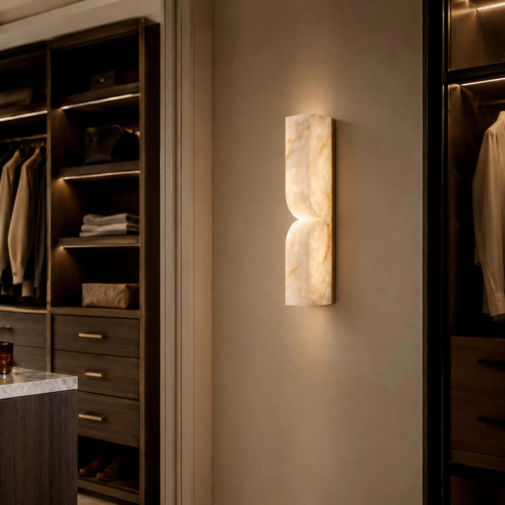 Cavira alabaster wall sconce providing warm accent light between dark built-in wardrobes in a walk-in closet