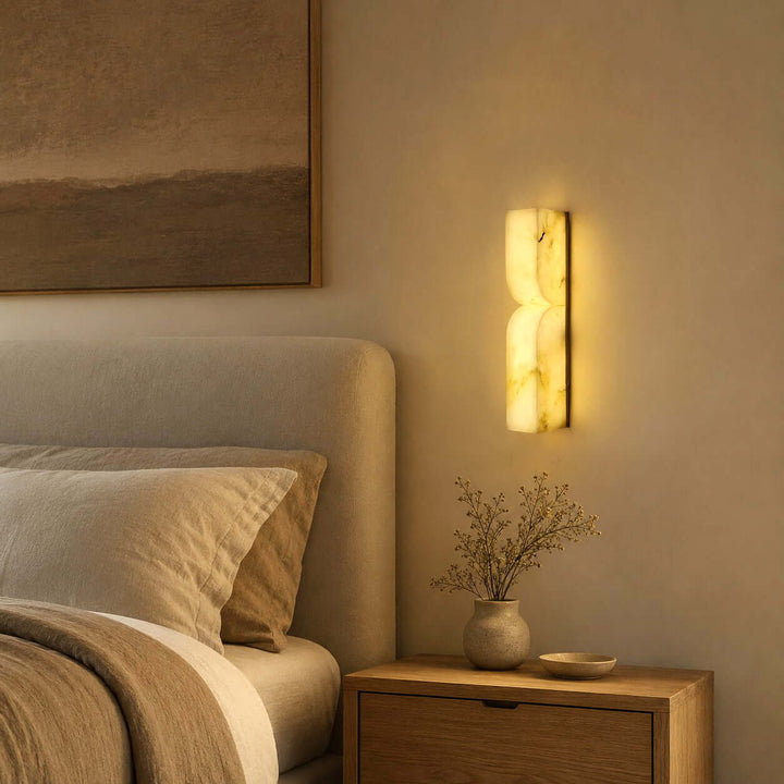 Cavira alabaster wall sconce providing warm bedside light above a wood nightstand in a neutral bedroom