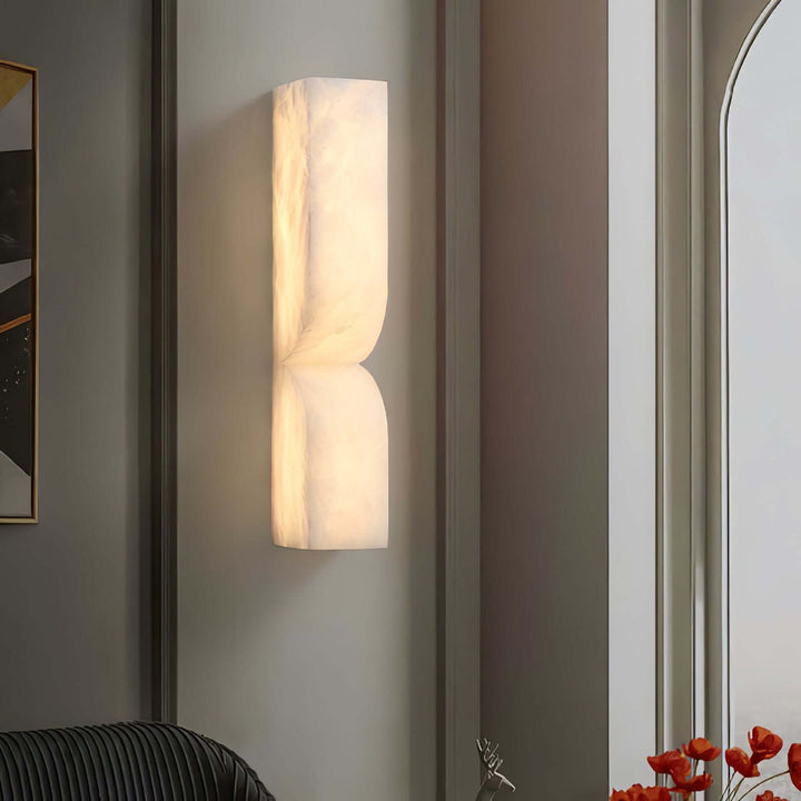 Cavira alabaster wall sconce glowing against a dark paneled wall beside an arched window