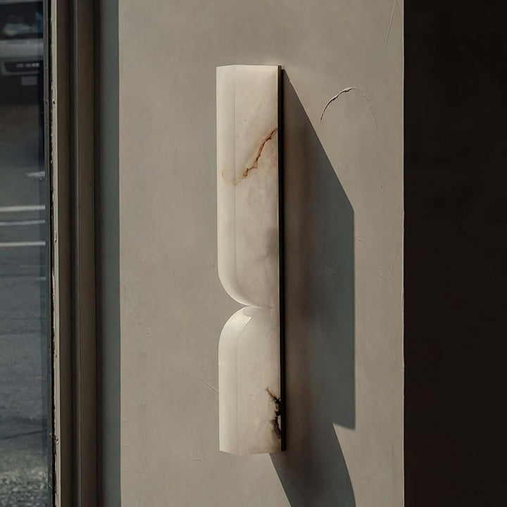 Unlit Cavira alabaster wall sconce shown at an angle in natural sunlight with a strong wall shadow