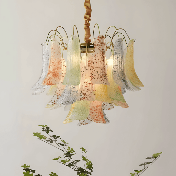 Illuminated colorful Murano glass chandelier displayed against a neutral wall with greenery