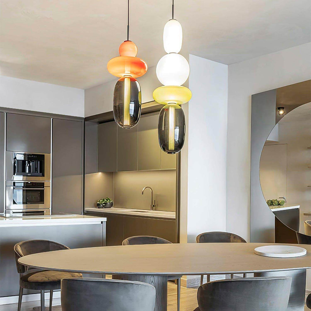 Two colorful glass pendant lights above an oval dining table beside a modern kitchen