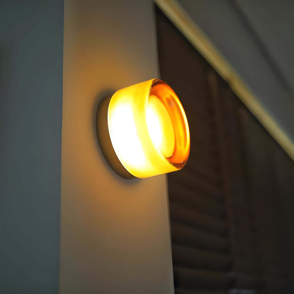 Amber glass wall sconce glowing on a stair wall with warm light and a clear side profile.