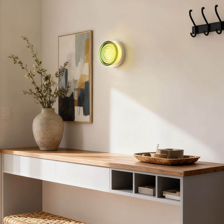 Green round glass wall sconce above an entry console with framed art and wall hooks.