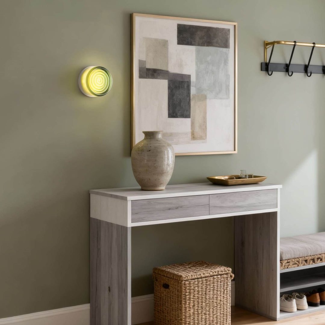 Green glass wall sconce with concentric front detail above a console table in an entryway.