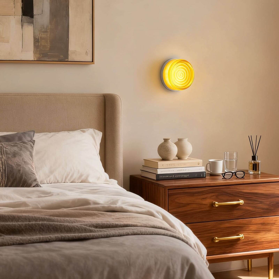Amber round glass wall sconce above a wood nightstand in a warm bedroom setting.