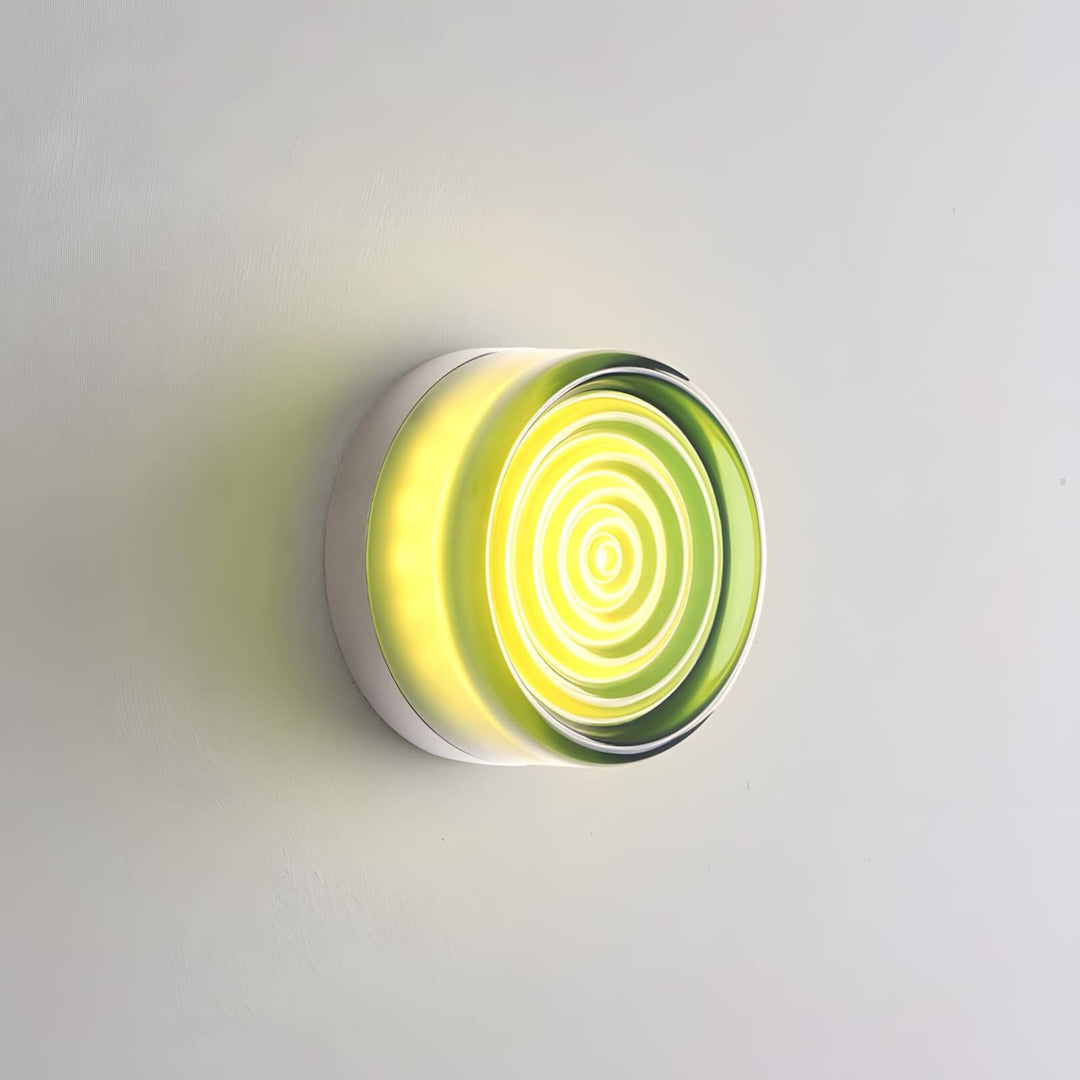 Green glass wall sconce with concentric front rings and warm center light on a gray wall.