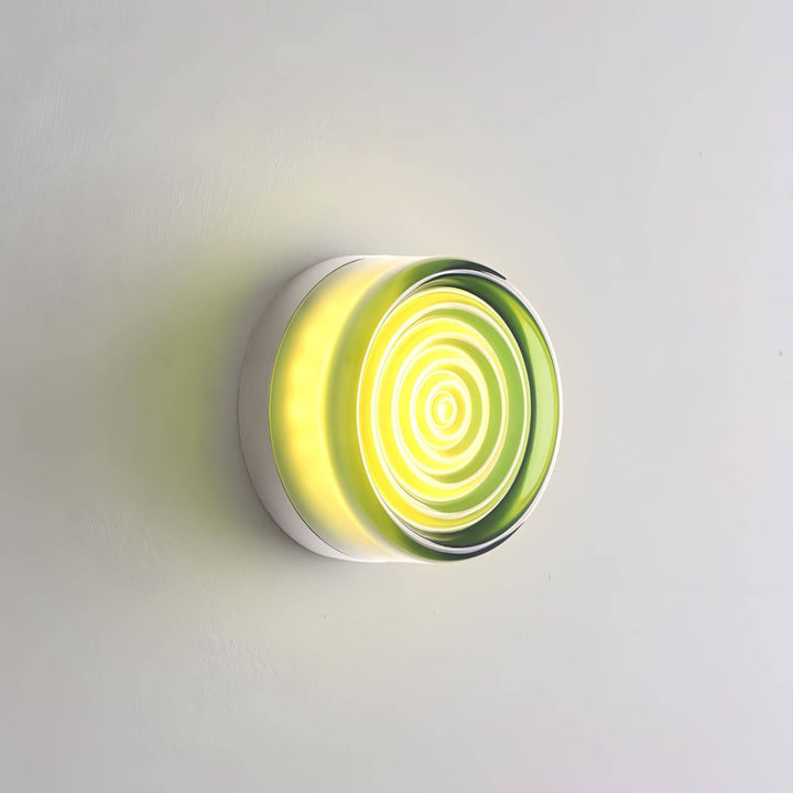 Green glass wall sconce with concentric front rings and warm center light on a gray wall.