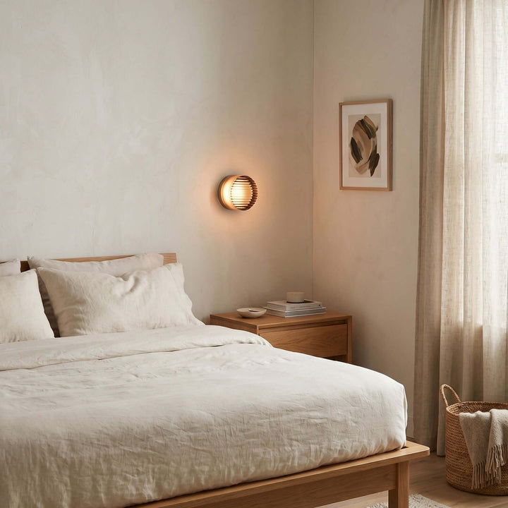Dimple wall sconce glowing above a bedside table in a neutral bedroom.