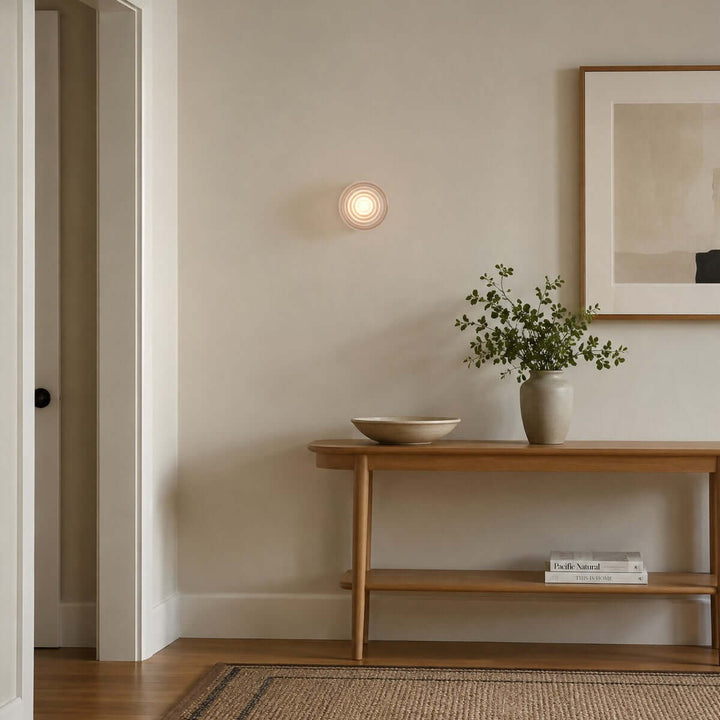 Dimple wall sconce above a wood entry console with framed wall art.