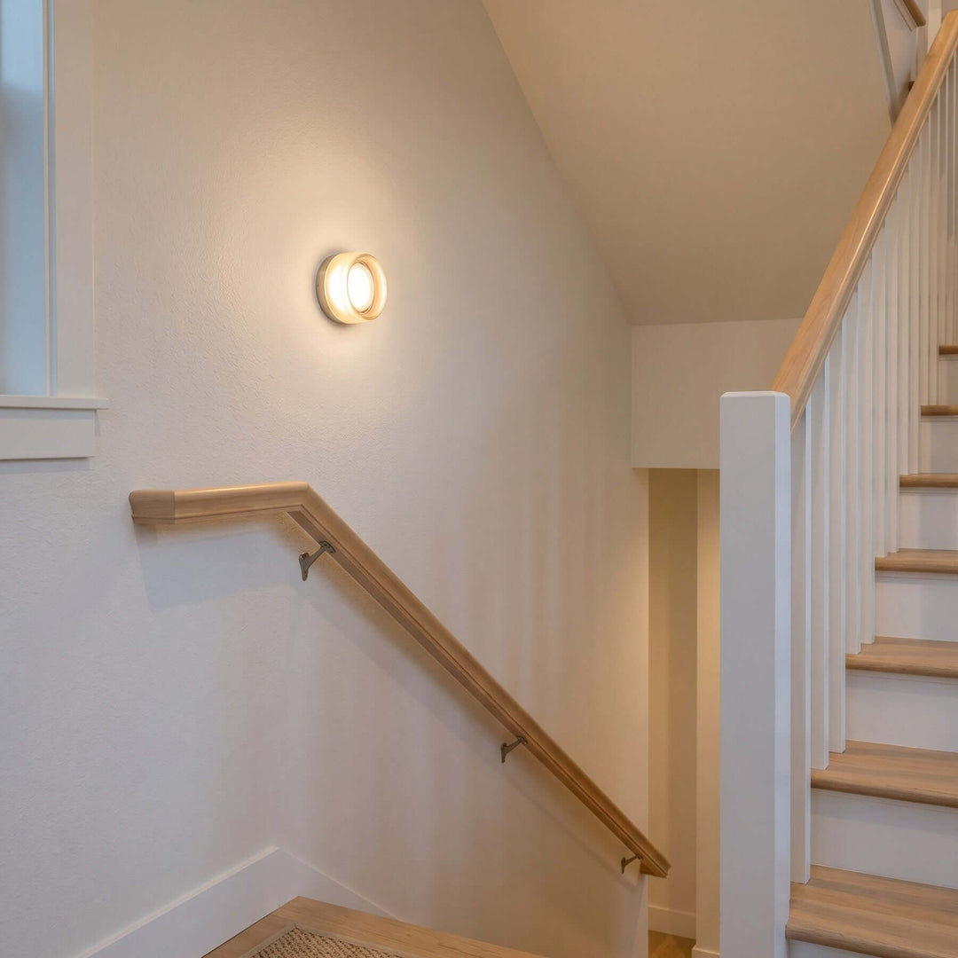 Dimple wall sconce glowing beside a staircase handrail.
