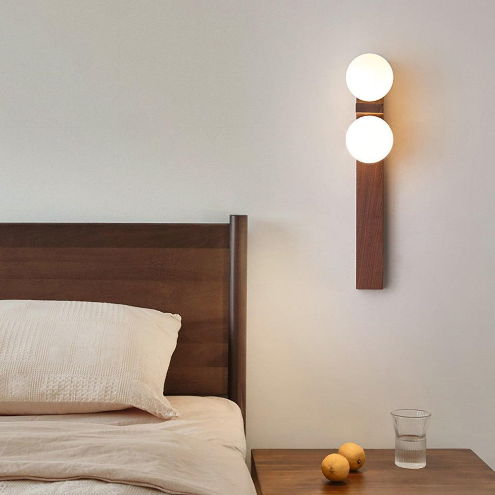 Eveline double wall sconce lit beside a wooden bed and nightstand in a calm bedroom setting