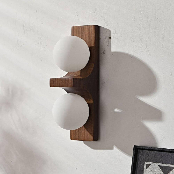 Dark wood double wall sconce with two white glass globes mounted on a textured wall with shadow