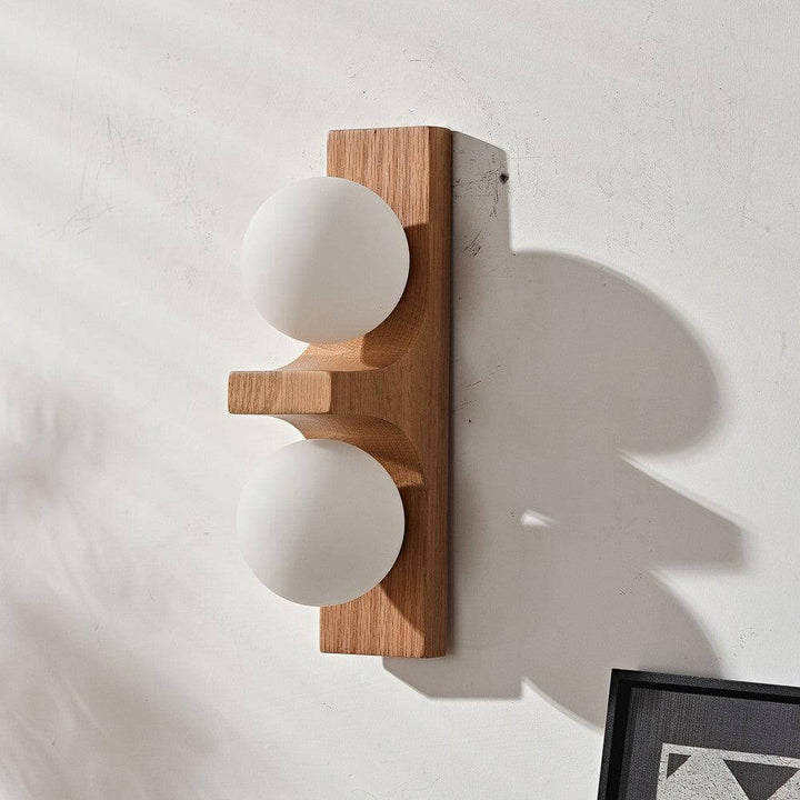 Light wood double wall sconce with two white glass globes on a textured wall with soft shadow