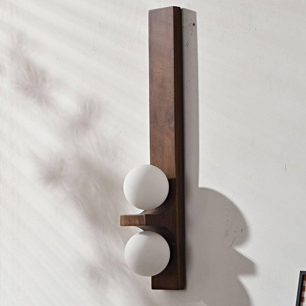 Tall dark wood double wall sconce with two white glass globes shown unlit on a white wall