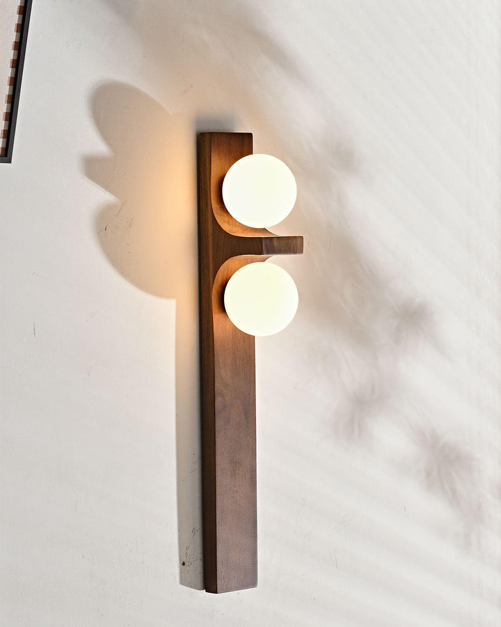 Tall wood double wall sconce viewed from above with two lit globes and a warm wall shadow