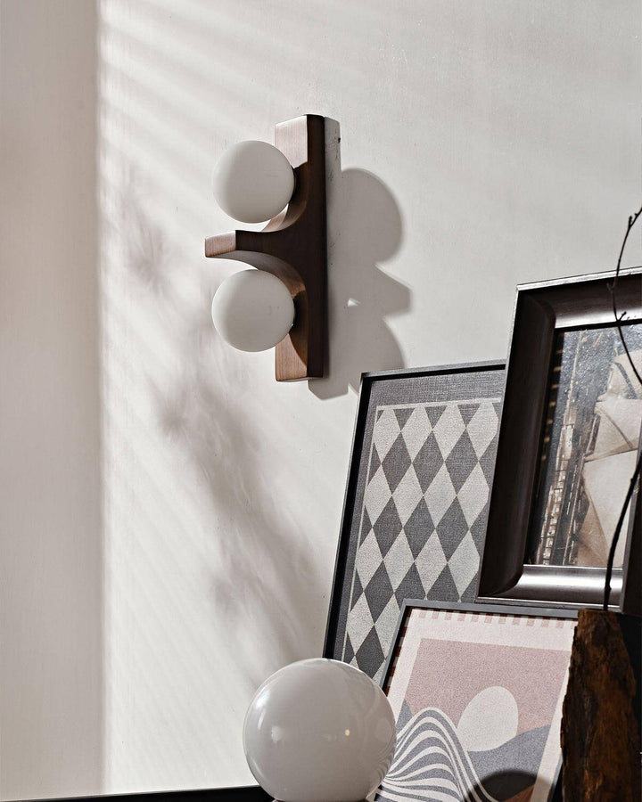 Short dark wood double wall sconce mounted above framed art in a softly shadowed wall scene