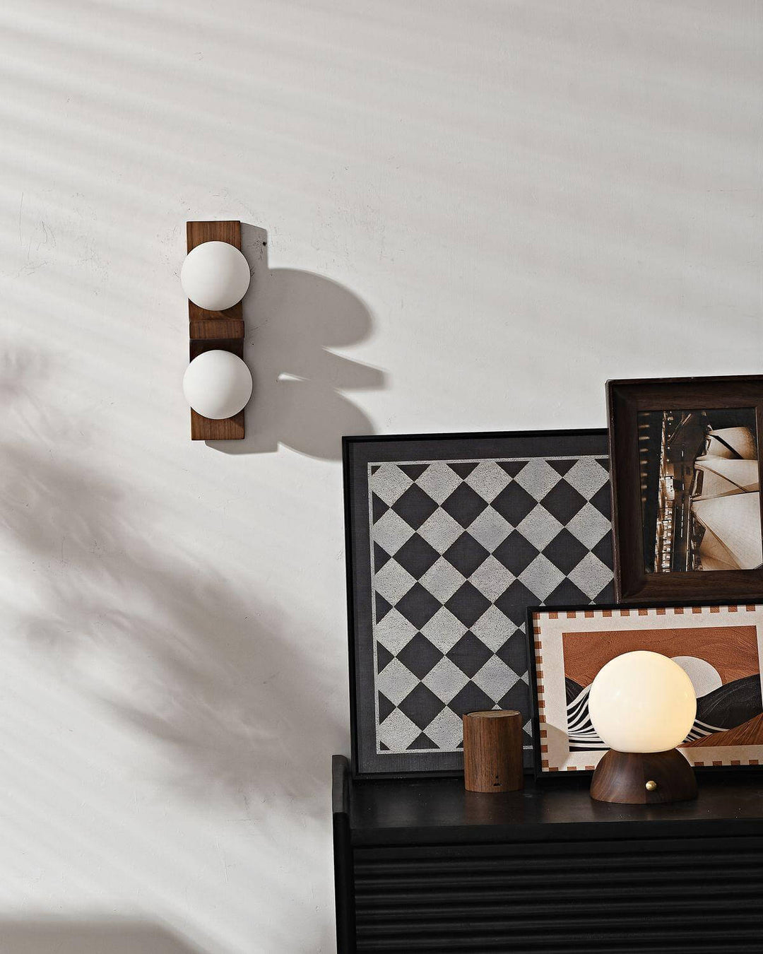 Short dark wood double wall sconce shown unlit above cabinet decor and framed artwork