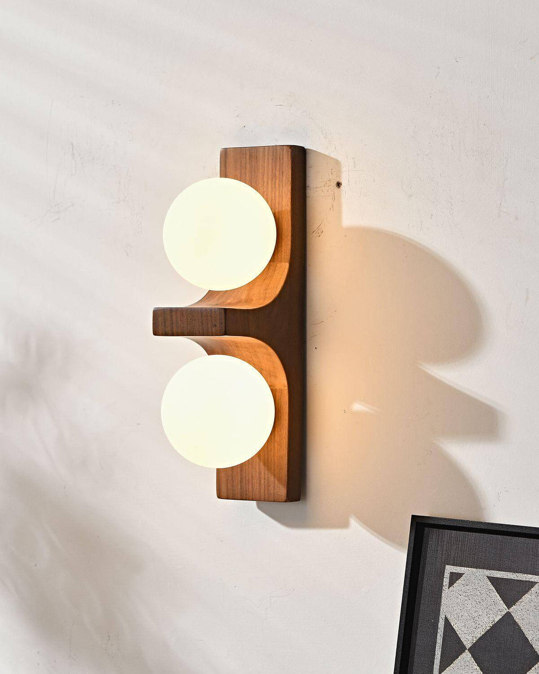 Short wood double wall sconce with two glowing white globes and warm wall shadow close up