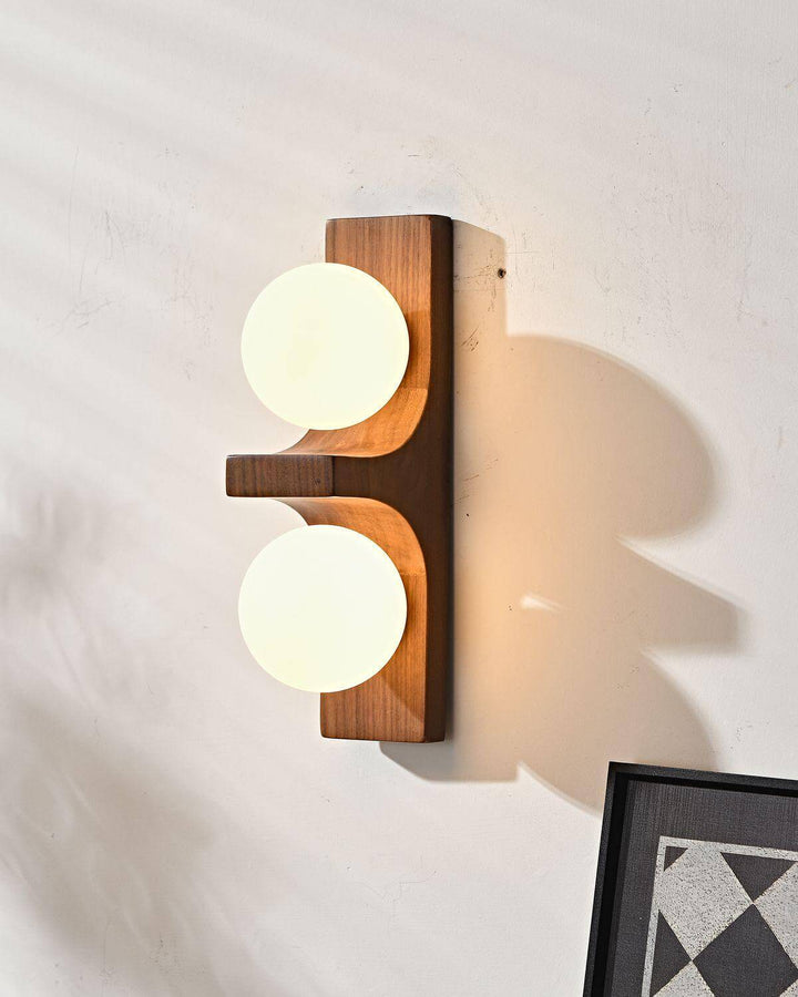 Short wood double wall sconce with two glowing white globes and warm wall shadow close up