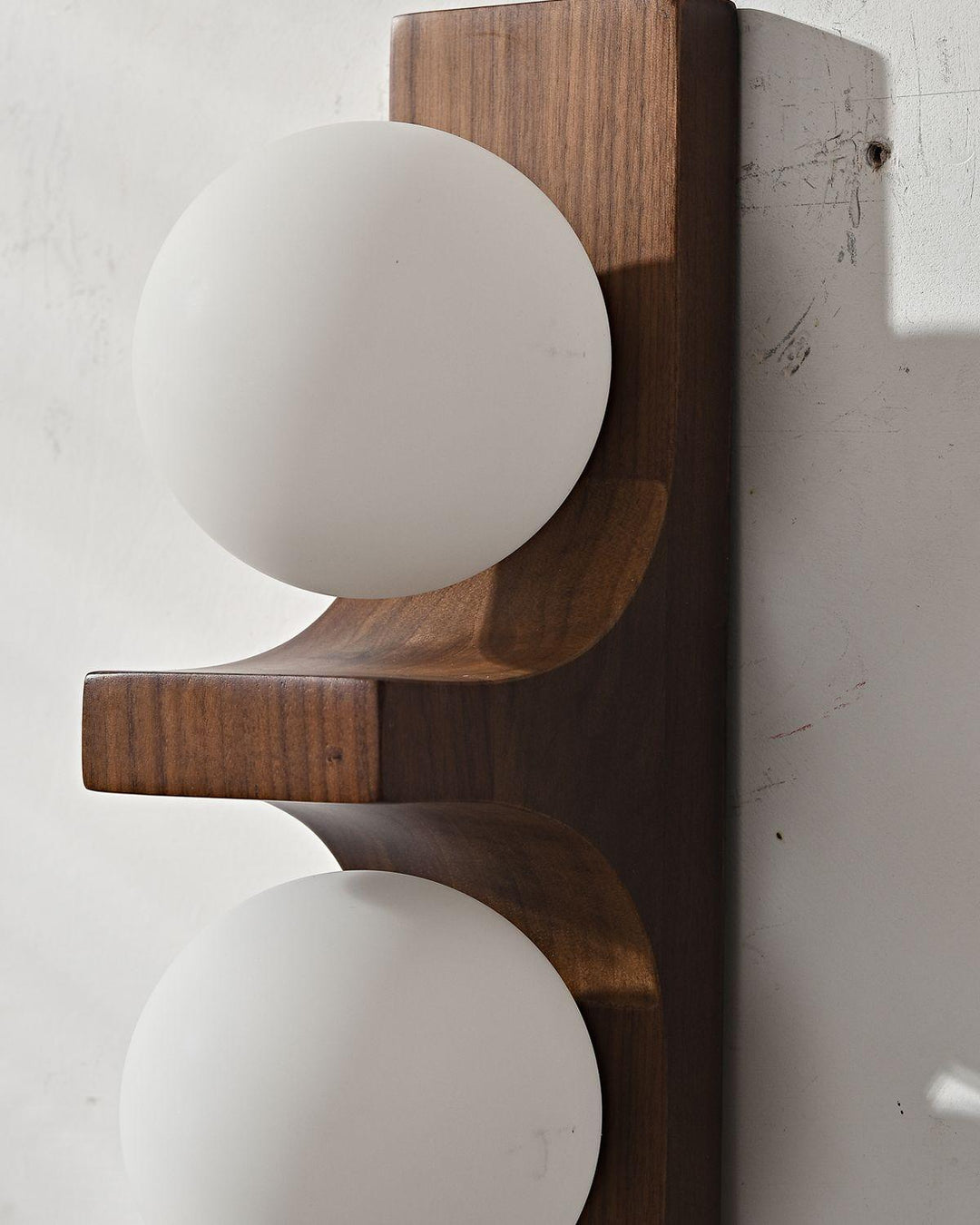 Close view of dark wood double wall sconce with white glass globes and visible wood grain
