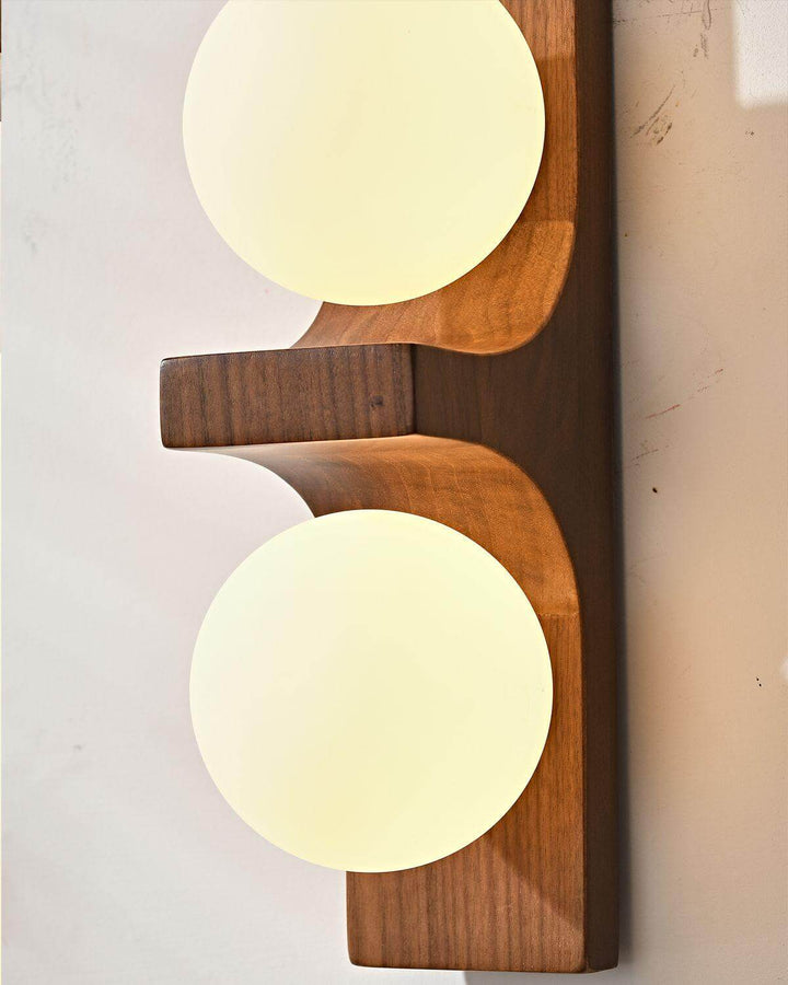 Close view of glowing white glass globes and curved wood support on the double wall sconce