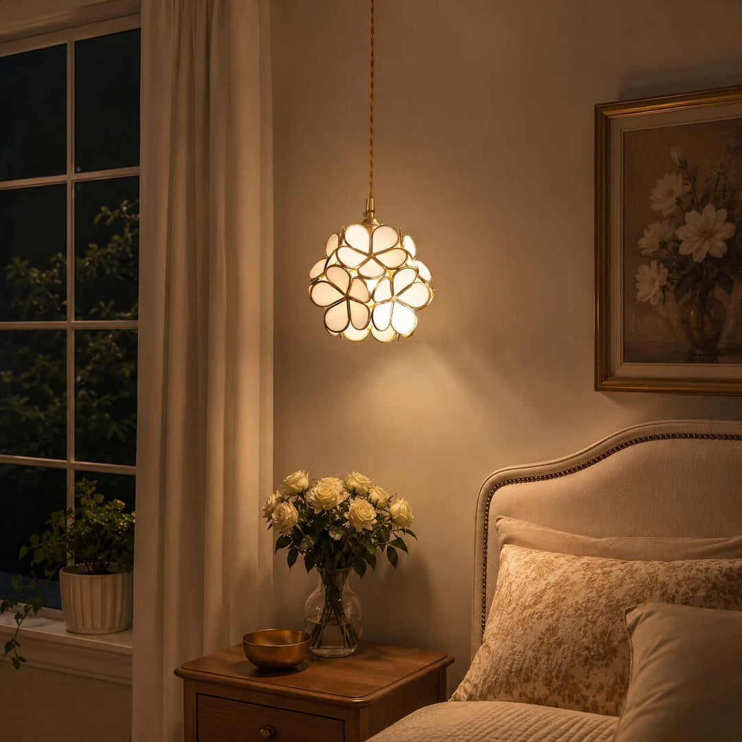 White glass petal pendant light glowing warmly above a bedroom nightstand at night
