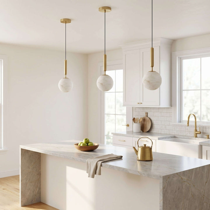 Three alabaster kitchen island hanging lights with brass stems in a bright white kitchen