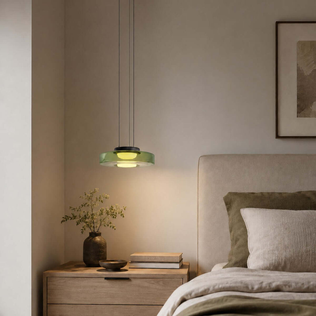 Green one-layer glass pendant light suspended above a bedroom nightstand beside a neutral bed