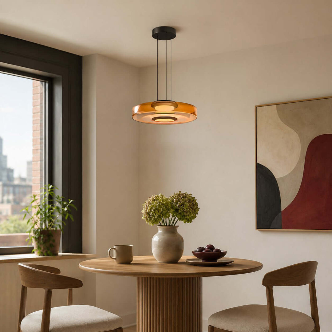 Orange one-layer glass pendant light above a compact round dining table with modern artwork